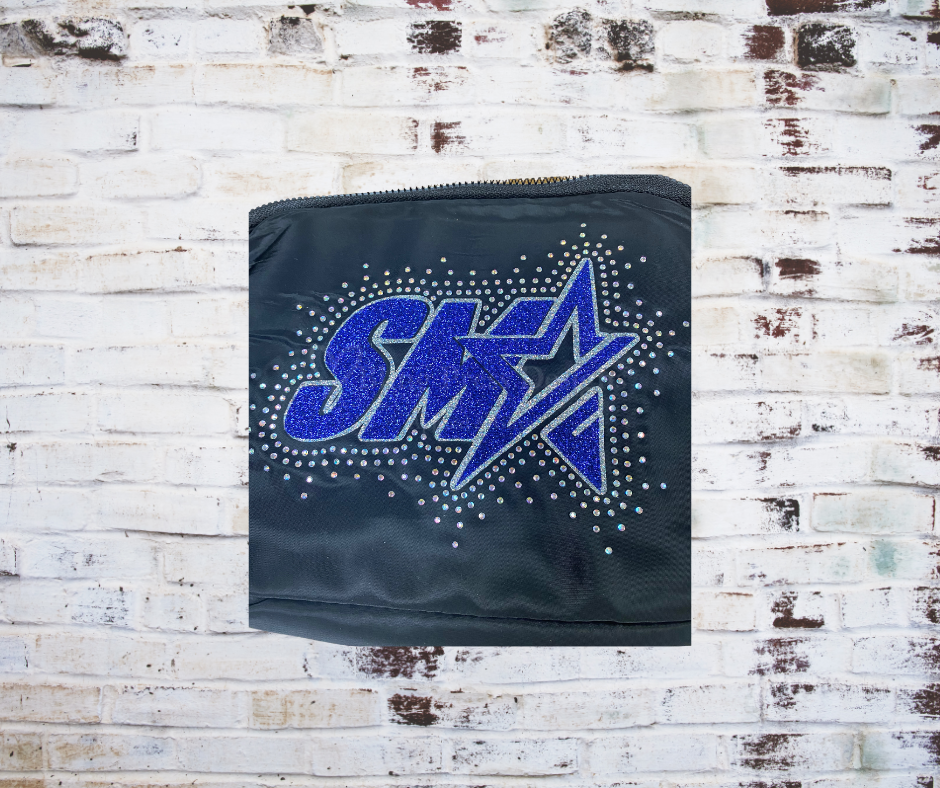 A close up of the Glitter SMA Logo with Rhinestone Scatter Cross Body Bag, featuring a sparkling SMA logo surrounded by rhinestones. A stylish and functional accessory with an adjustable strap, perfect for carrying essentials with a touch of glamour.