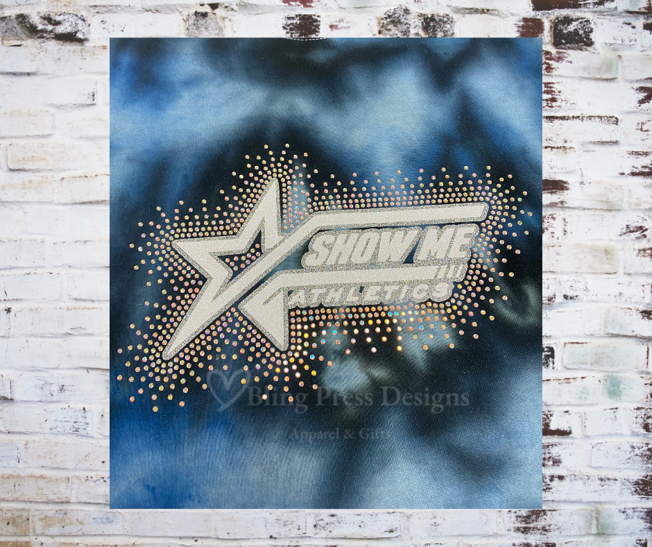 A close up of a Tie Dye Sweatshirt featuring a glitter Show Me Athletics logo with a scatter of rhinestones, adding sparkle and shimmer.