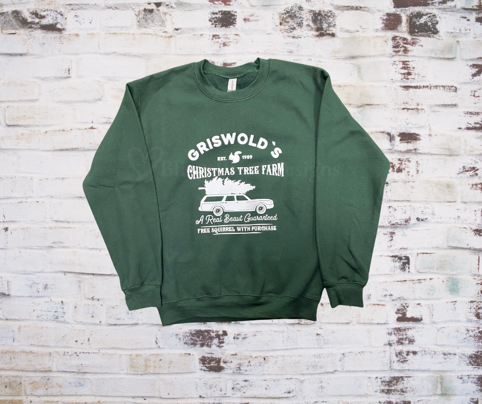 A green crewneck sweatshirt with 'Griswold's Christmas Tree Farm' printed on the front, displayed on a brick wall background.