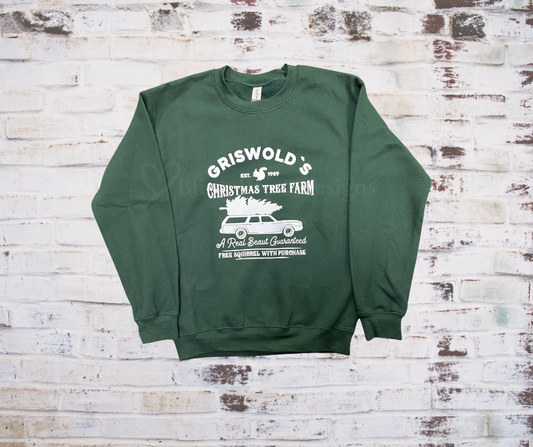 A green crewneck sweatshirt with 'Griswold's Christmas Tree Farm' printed on the front, displayed on a brick wall background.