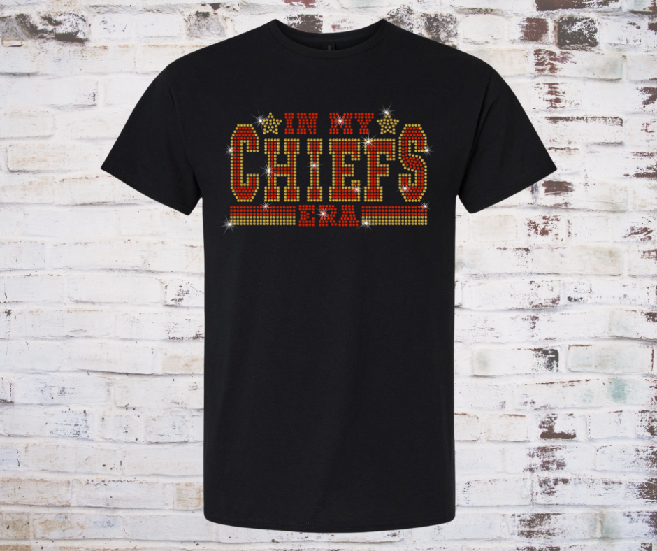 Black t-shirt with 'In My Chiefs Era' rhinestone text on a wooden background