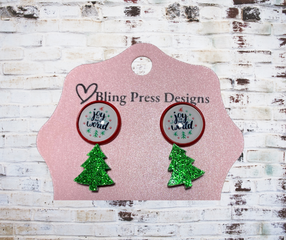 Earrings with Christmas tree designs on a Bling Press Designs card against a wooden background
