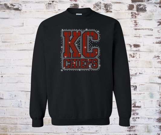Shirt covered in sparkling rhinestones featuring a full KC Chiefs scatter design. The red, gold, and clear rhinestones shimmer across the entire shirt, creating a bold and eye-catching game day look full of team spirit.