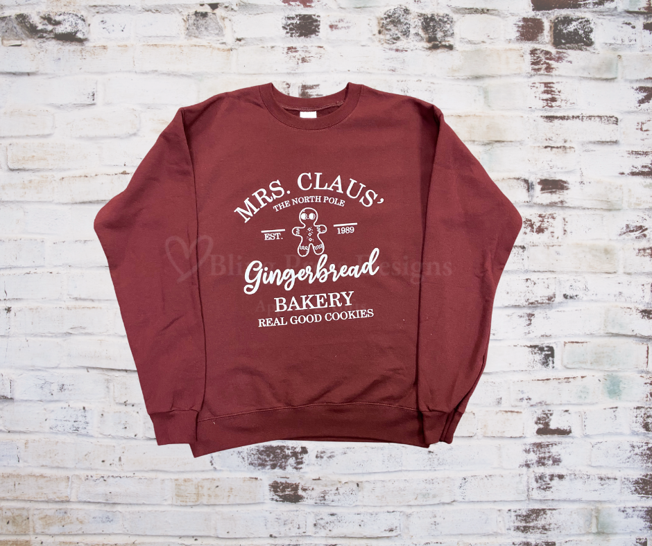 Holiday sweatshirt with a festive print that reads βMrs. Clause Gingerbread Bakeryβ featuring Christmas-themed design details.