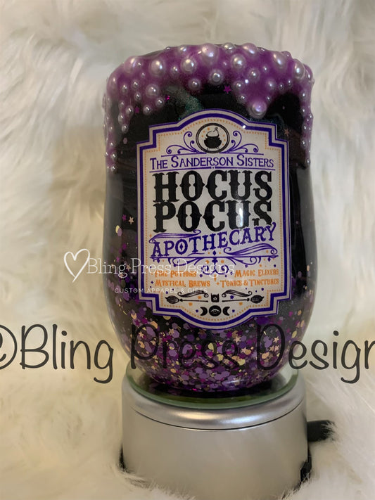 Decorative wine tumbler with 'Hocus Pocus Apothecary' label and purple beads on a white fur background.