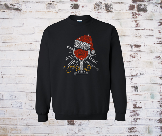 Black sweatshirt with a rhinestone wine glass and Santa hat design on a textured white brick wall.