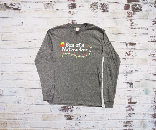 A **Son of a Nutcracker Long Sleeve Tee** featuring the playful phrase "Son of a Nutcracker" in bold lettering. Made from soft, breathable fabric for a comfortable, festive look during the holiday season.