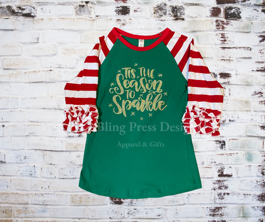 A festive "Tis' The Season to Sparkle" tee featuring candy striped ruffled 3/4 length sleeves and decorated with glitter vinyl, perfect for adding sparkle to holiday celebrations.