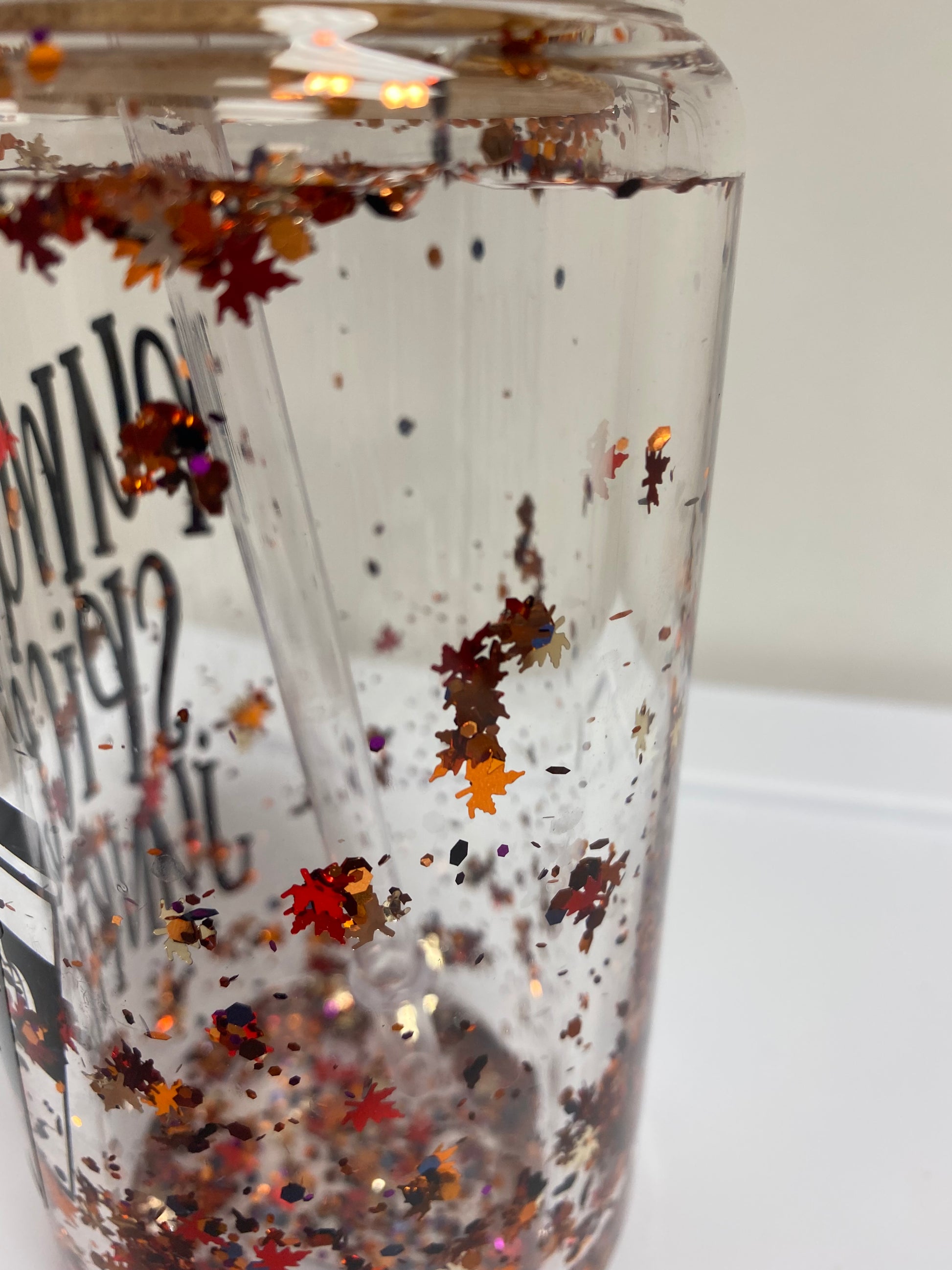 A close up of the Pumpkin Spice Snow Globe Glass Can Tumbler, featuring a festive snow globe design with pumpkin spice accents inside. Made from durable glass with a secure lid and straw, perfect for enjoying seasonal beverages.