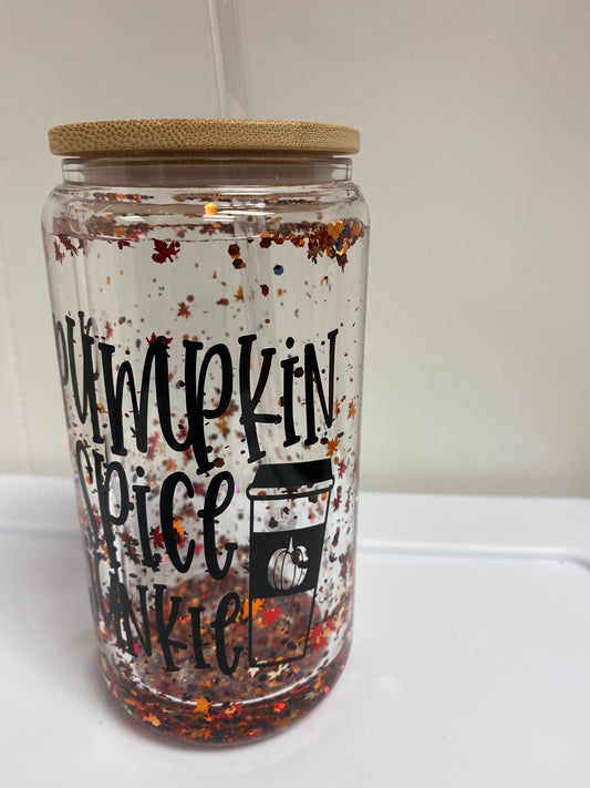 A Pumpkin Spice Snow Globe Glass Can Tumbler, featuring a festive snow globe design with pumpkin spice accents inside. Made from durable glass with a secure lid and straw, perfect for enjoying seasonal beverages.
