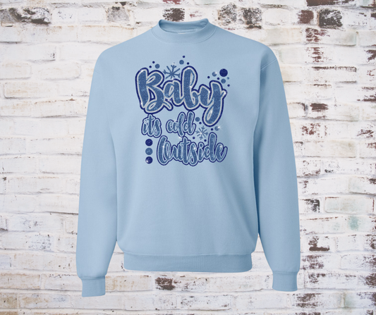 Light blue sweatshirt with text 'Baby it's cold outside' on a wooden background