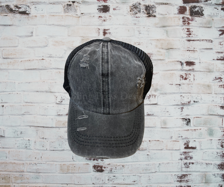 A distressed criss cross ponytail hat with a breathable design, adjustable Velcro strap, and elastic back openings for high, mid, or low ponytails, perfect for casual wear and customization.