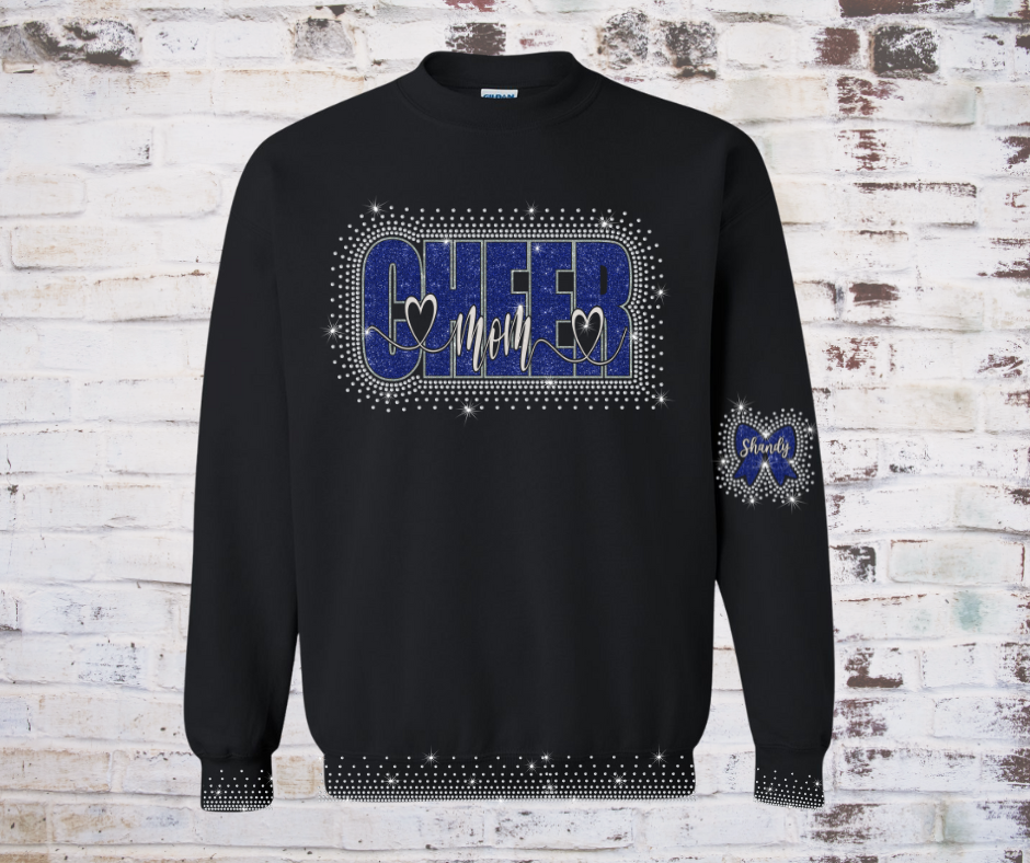 Cozy sweatshirt featuring a rhinestone and glitter “Cheer Mom” design with a cheer bow, personalized with the athlete’s name, and sparkling rhinestone accents along the sleeve cuffs and waistline.