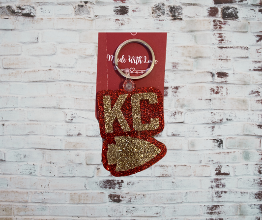 A glitter acrylic keychain featuring a bold "KC" design, perfect for Kansas City fans, with a sparkling finish and durable, lightweight construction.