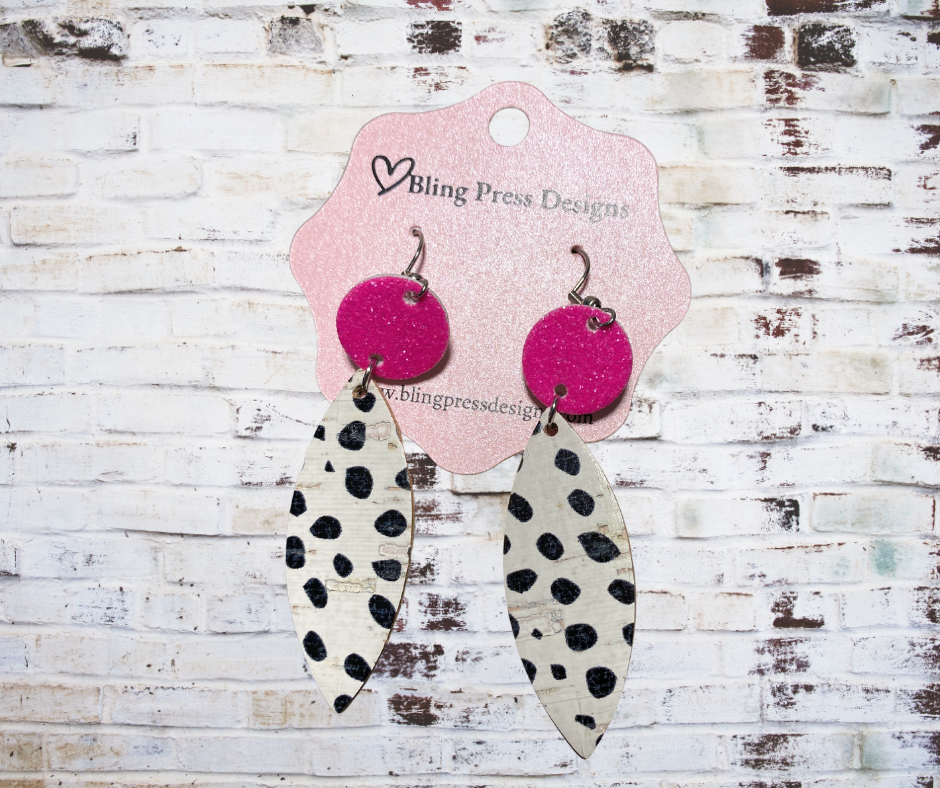 Pair of earrings with pink circular tops and black and white leaf-shaped bottoms on a Bling Press Designs card.