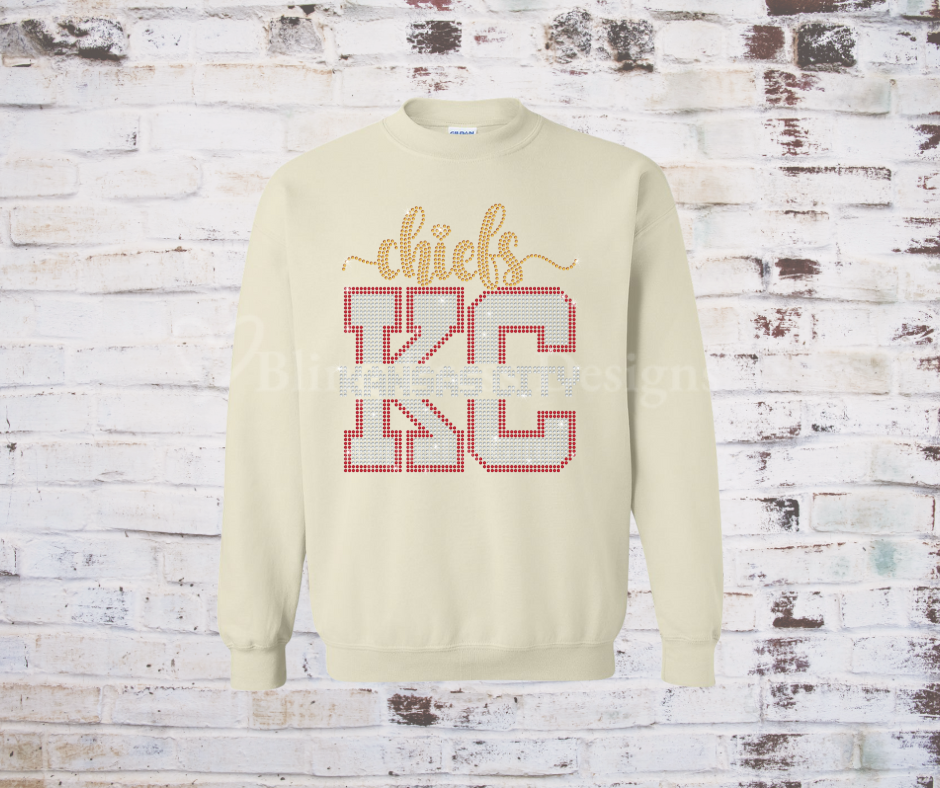 Close-up of a rhinestone KC sweatshirt, featuring sparkling rhinestones outlining the KC on a cozy, casual Cream Colored Sweatshirt