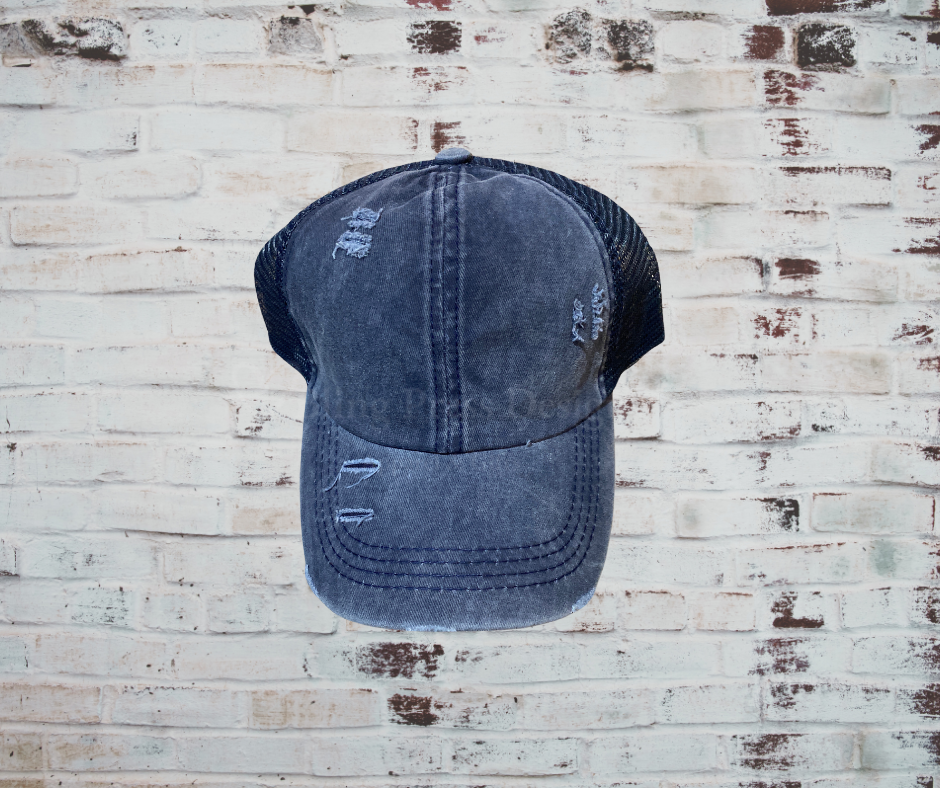 A distressed criss cross ponytail hat with a breathable design, adjustable Velcro strap, and elastic back openings for high, mid, or low ponytails, perfect for casual wear and customization.