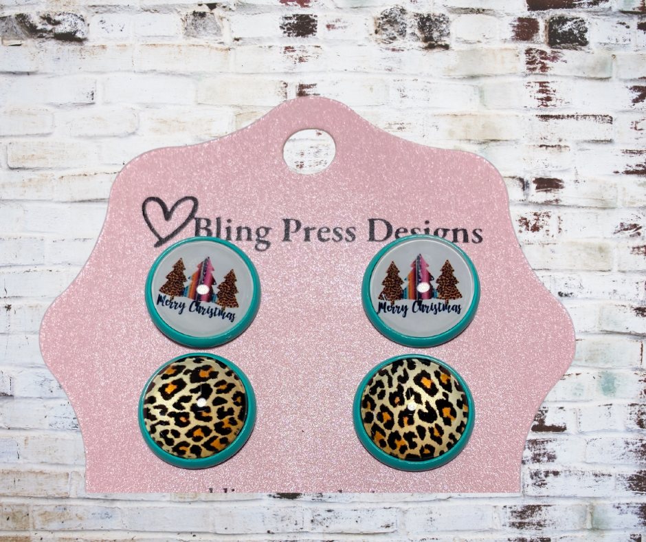 Four Christmas-themed earrings on a Bling Press Designs card against a rustic wooden background.