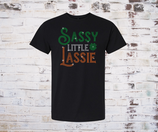 Black t-shirt with 'Sassy Little Lassie' rhinestone text on a wooden background