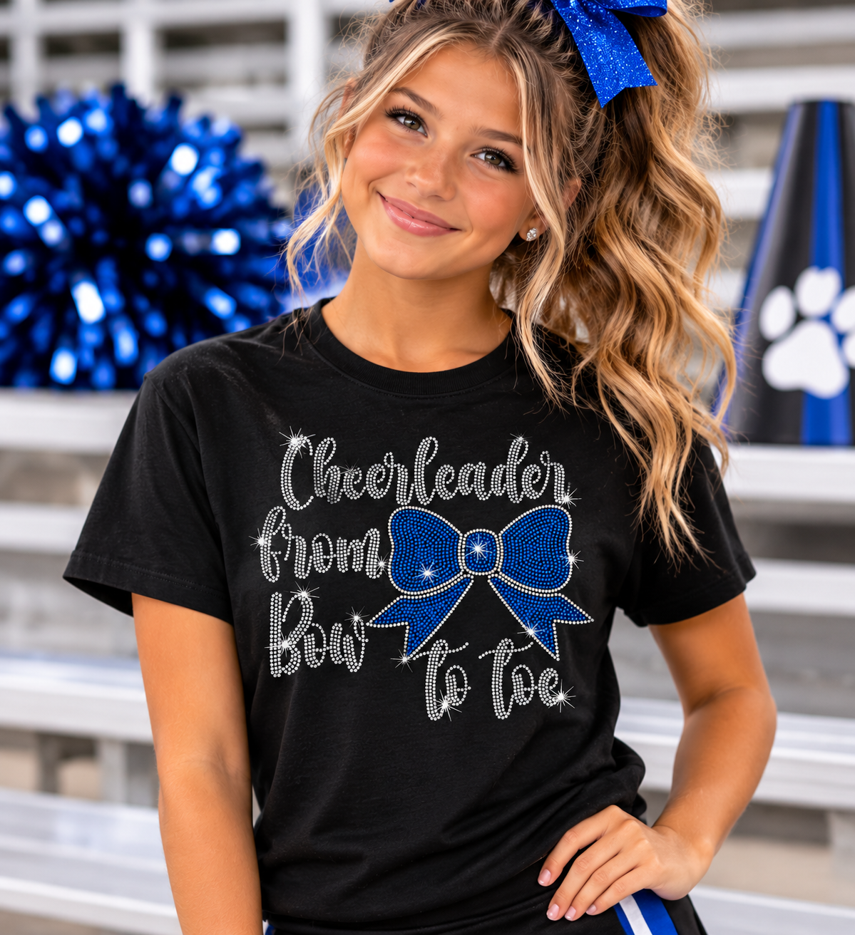  Cheerleader from Bow to Toe rhinestone design featuring sparkling silver lettering and a royal blue bow on a black Gildan Softstyle T-shirt, customizable to match team colors
