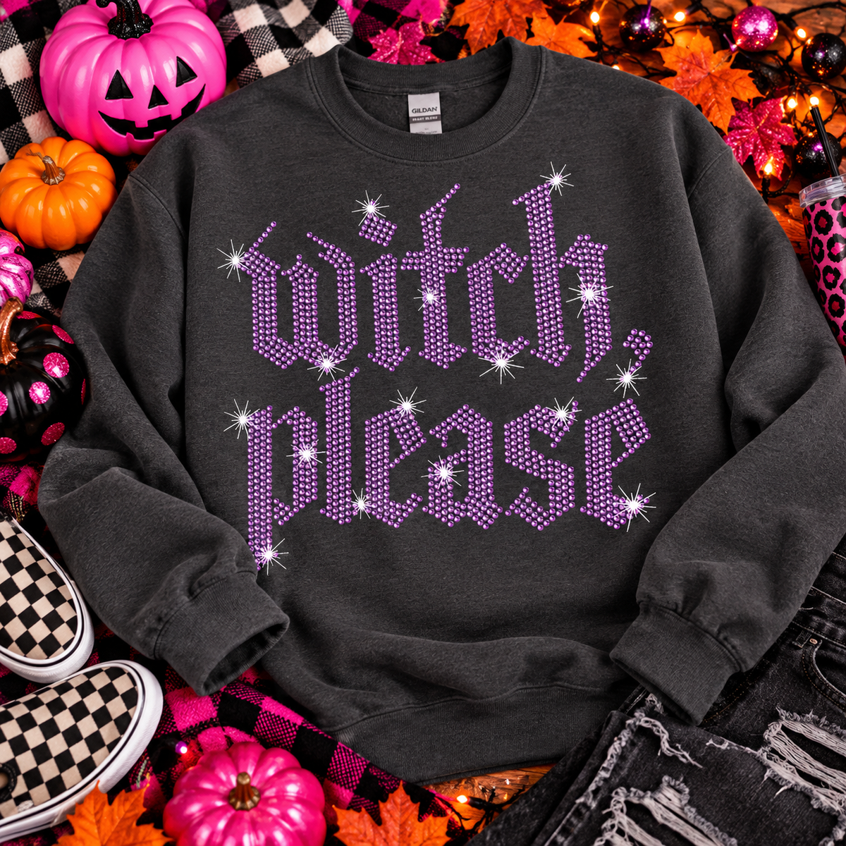 A dark charcoal gray sweatshirt with 'witch, please' in purple glitter-style lettering and white sparkle accents, styled in a Halloween flat lay with pumpkins, autumn leaves, string lights, jeans, and checkered sneakers.