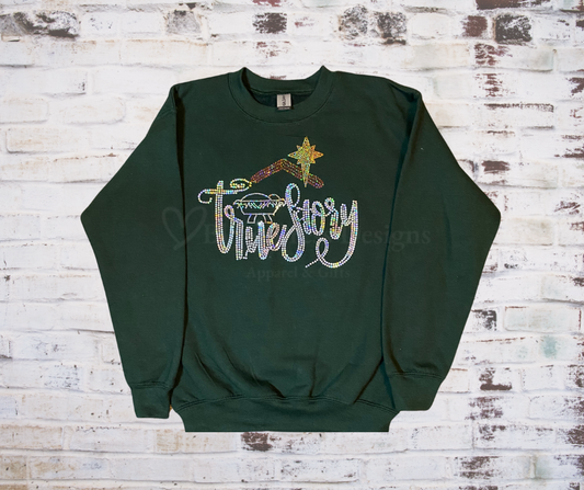 
**“Green sweatshirt with rhinestone design featuring Baby Jesus in a manger and the words ‘True Story.’”**


